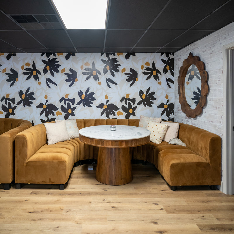 Brown sectional sofa with a round wooden table against a floral-patterned wall.