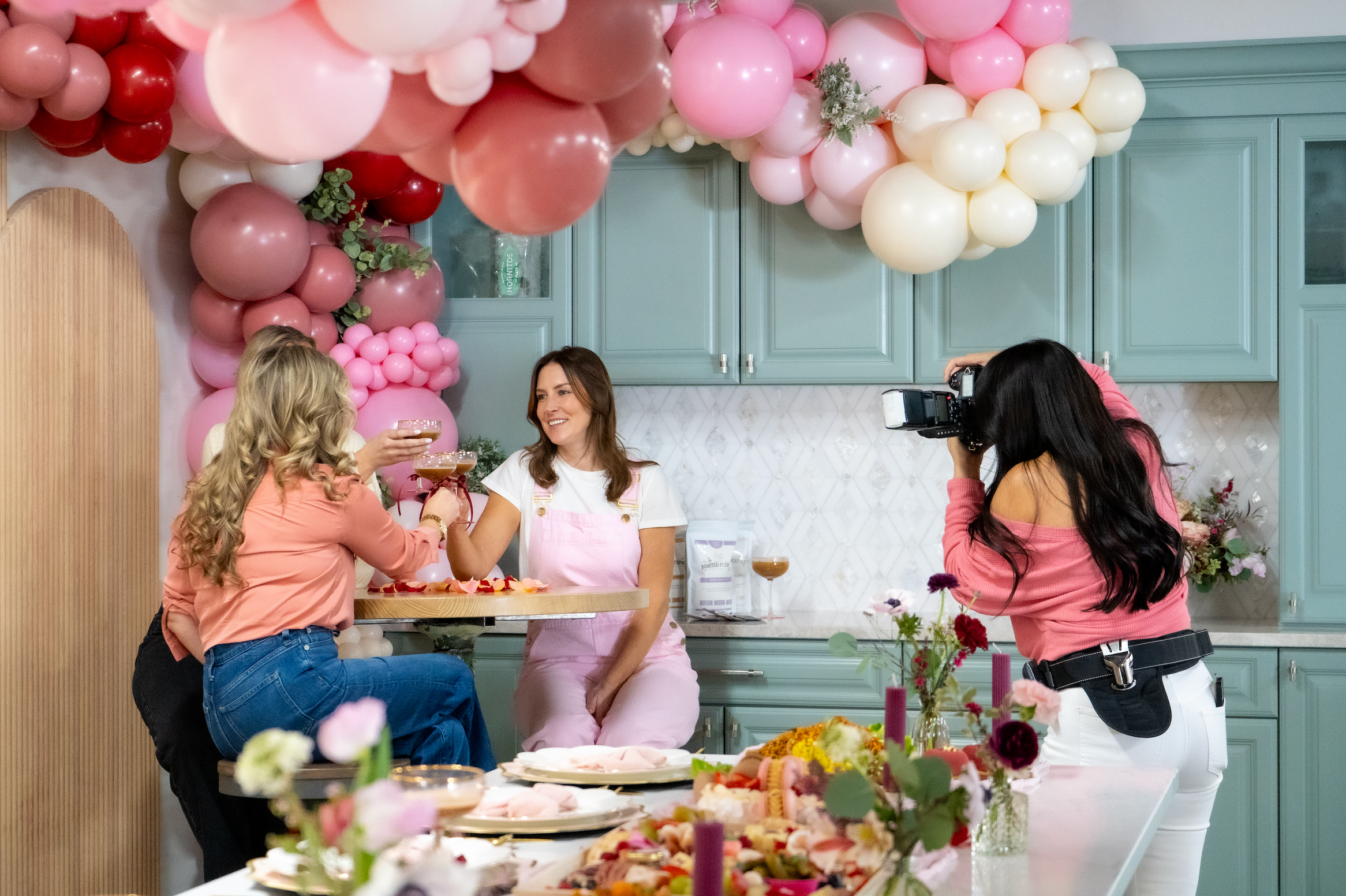 An image showing a group of people at a party or gathering, with balloons and food in the background. It appears to be a festive atmosphere.