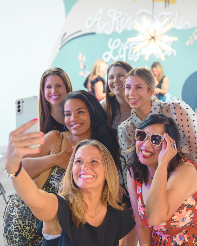 Group of women taking a selfie in front of a decorative wall 