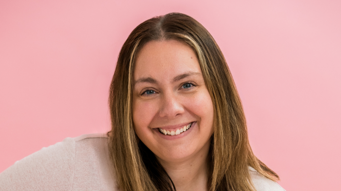 Woman with long blonde hair smiling against a pink background